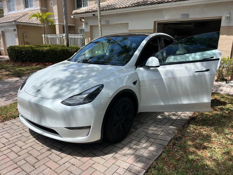 White Tesla Model Y in a driveway with the front door open showing tinted glass